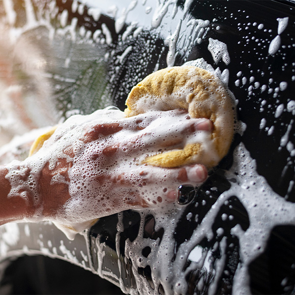 Hand washing car exterior with soap and sponge