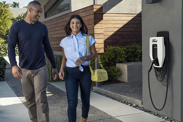 A couple walking out of their home with a Ford Charge Station Pro attached to their garage in the background