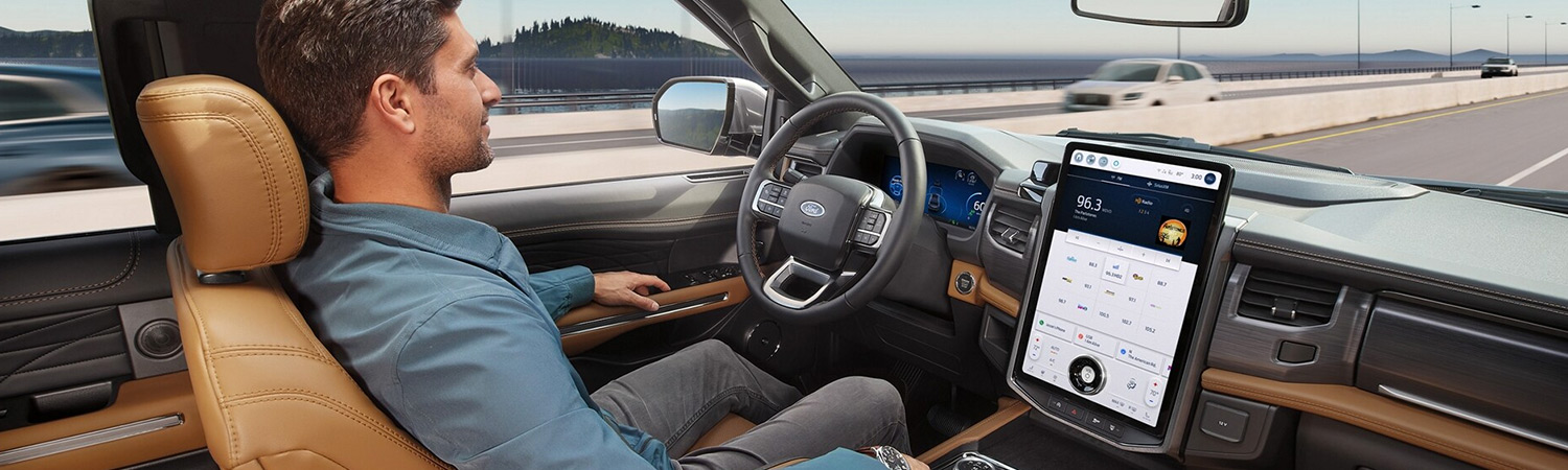 A man sits in the driver seat of a Ford Expedition SUV with his hands off the steering wheel while Ford BlueCruise is active.