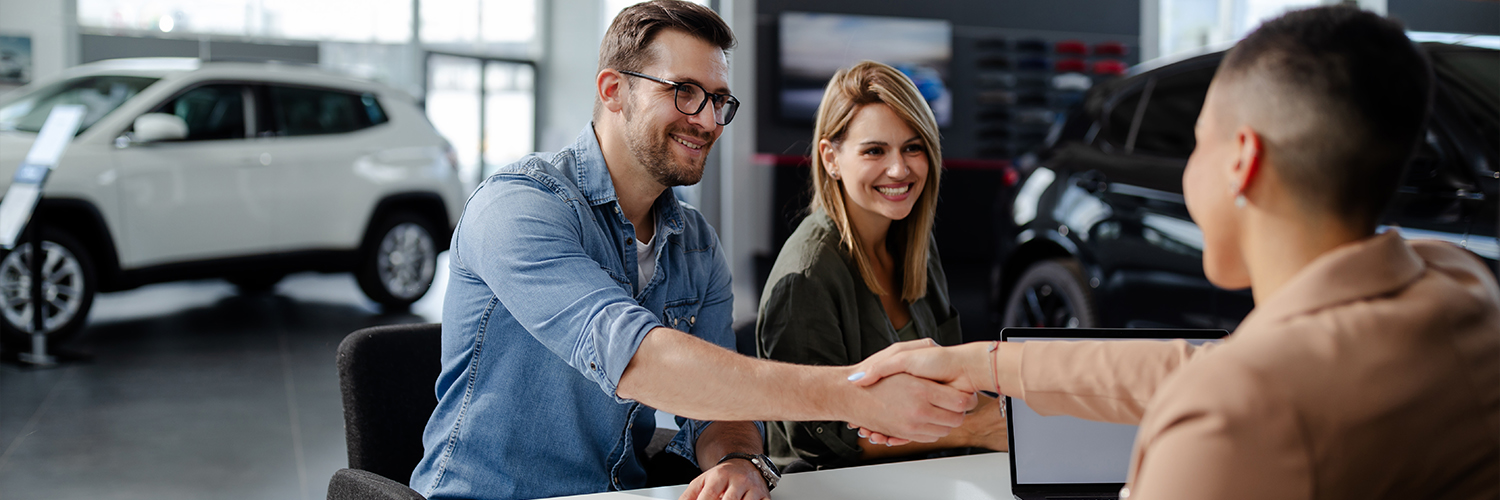 Male customer and female car dealer shaking hands at showroom.