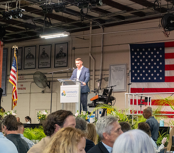 Man speaking at podium with US flag backdrop.