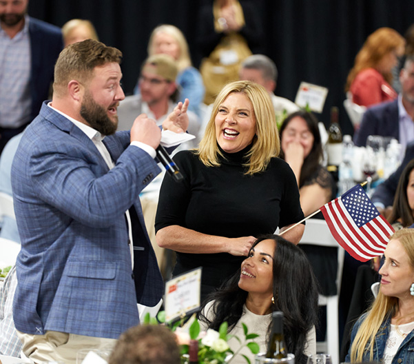 Man speaking with mic, woman laughing at event.