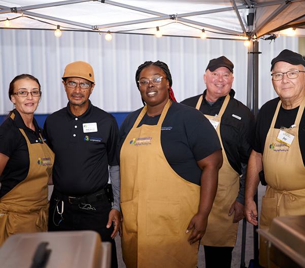 Five caterers in aprons posing at an event.