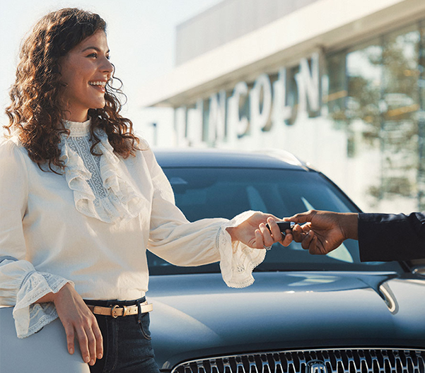Sales woman handing over keys standing in front of a Lincoln vehicle