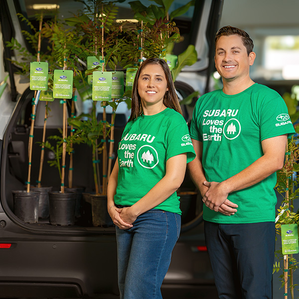 Two people in green shirts by a car with plants.