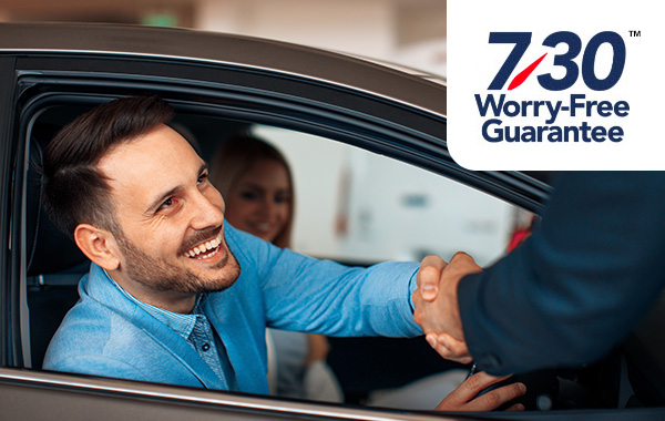 Customer smiling shaking hands with dealership employee with 7/30 Worry-Free Guarantee logo