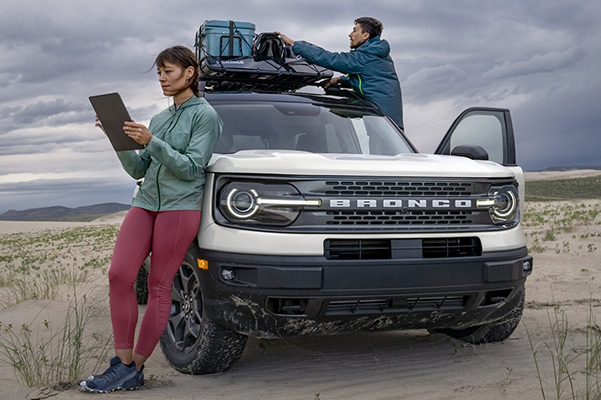 Ford Bronco Sport with lady leaning against it while man loads up the roof rack with luggage