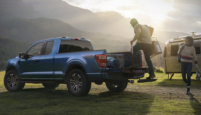 A couple loading camping gear into the bed of their 2021 Ford F 1 50 near their campsite