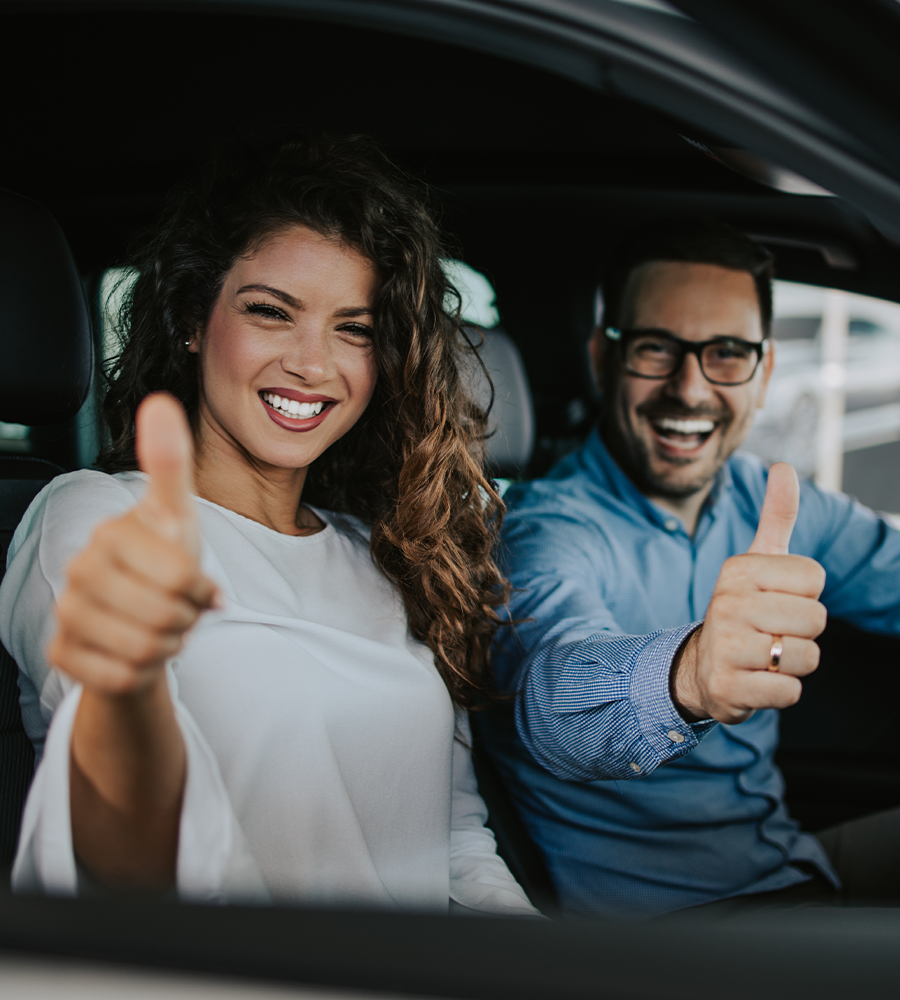 Happy middle age couple enjoying while choosing and buying new car at showroom.