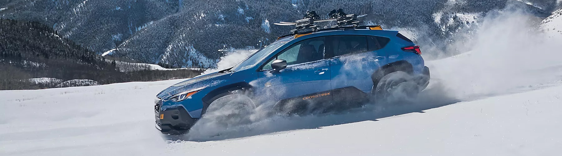 A blue Subaru Crosstrek Wilderness drives through deep snow in the mountains