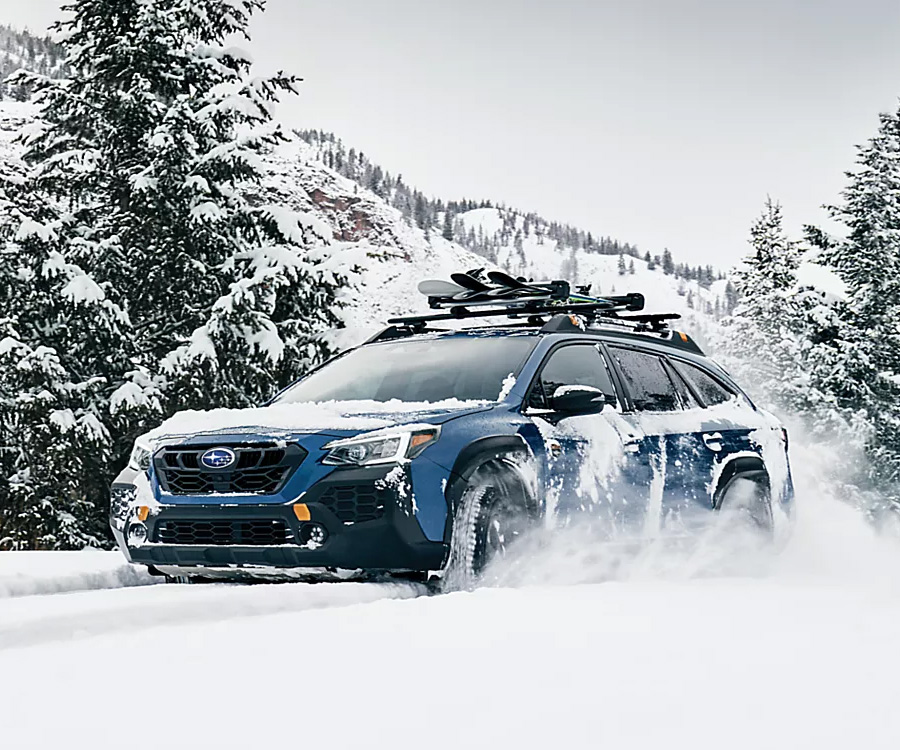 A Subaru Outback drives through deep snow on a mountain road