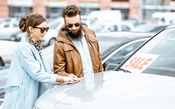 Young stylish couple choosing luxury car to buy on the open ground of the dealership